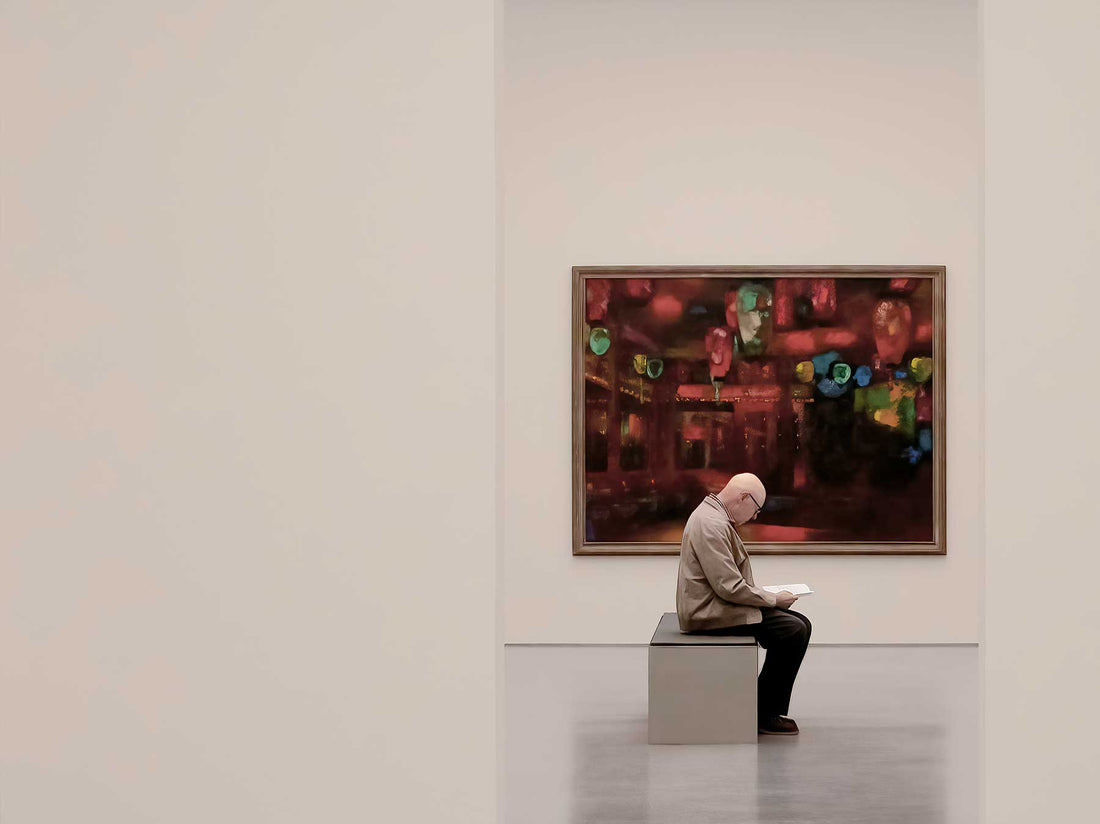A seated visitor looking at a single framed painting on a white gallery wall
