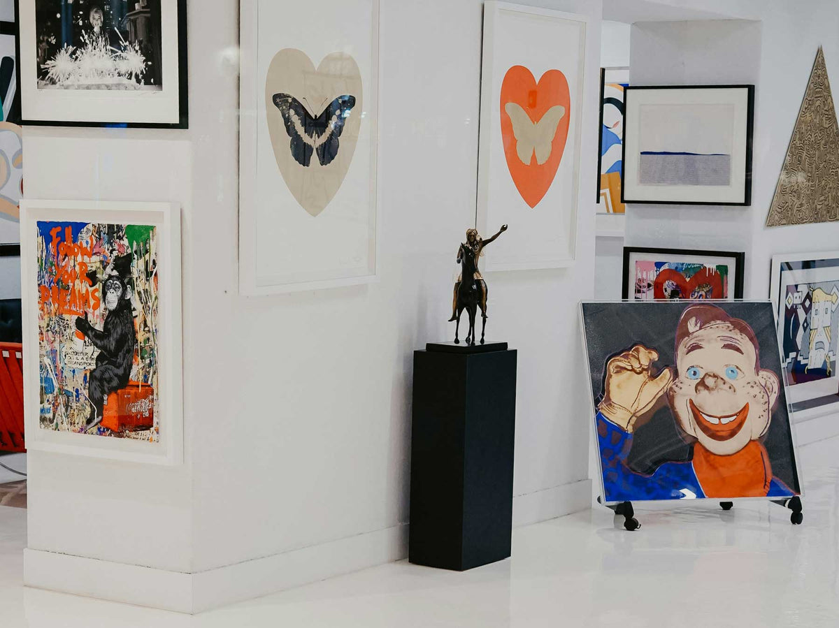 An art fair booth with paintings hung salon-style and a sculpture on a plinth