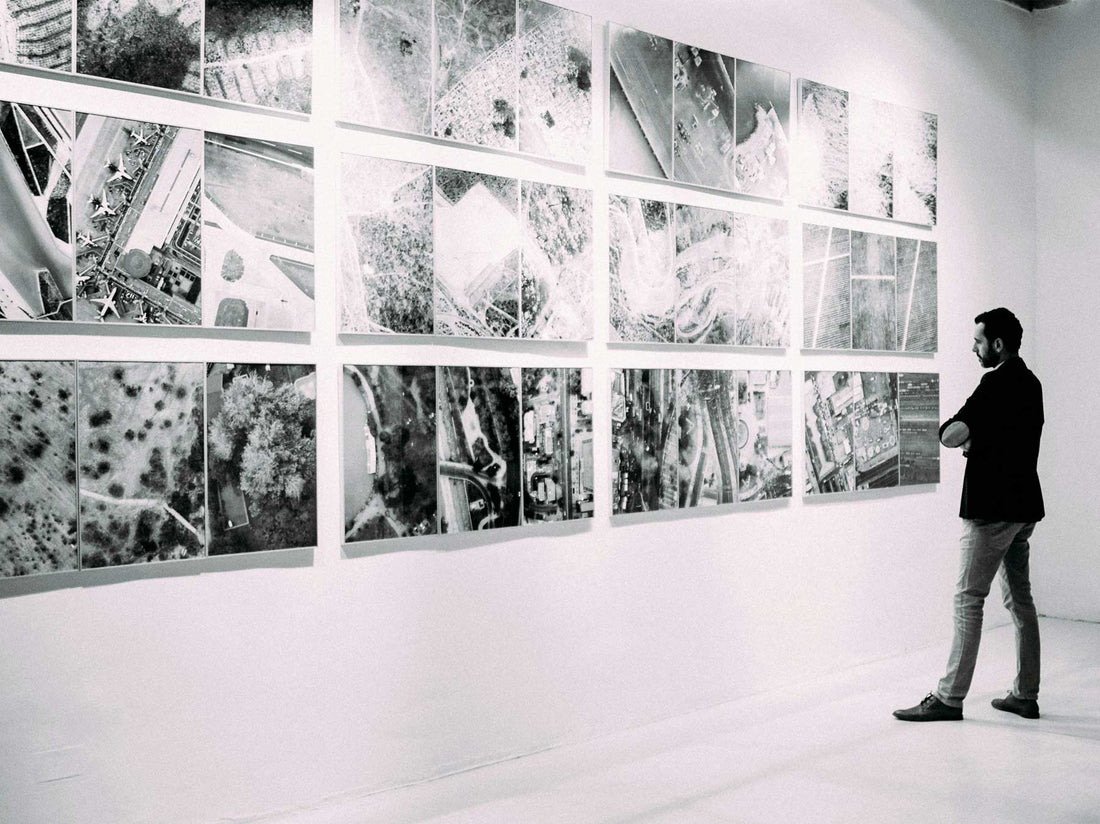 A visitor walking past a long wall of gridded black and white photographic works