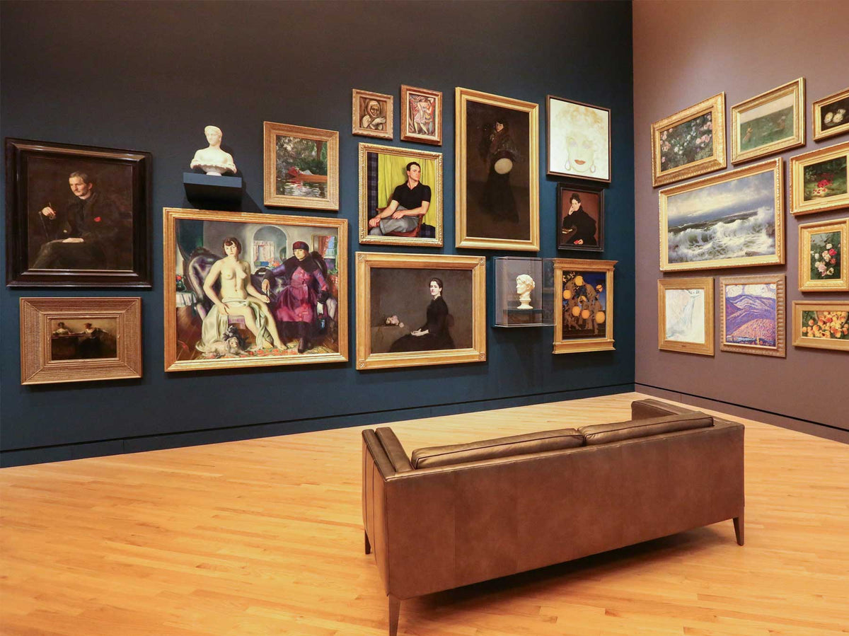 Historic paintings in ornate frames hung salon-style on a deep blue wall, with a bench
