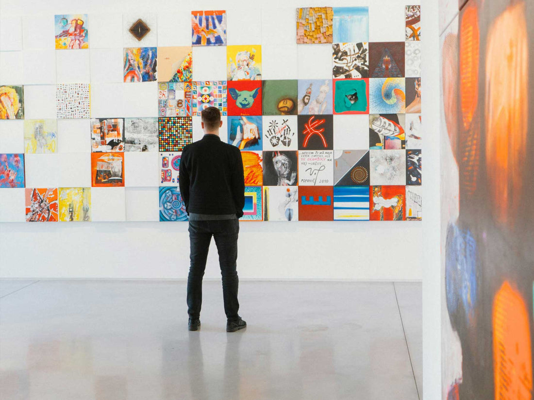 A visitor studying a dense grid of small contemporary works hung across a gallery wall