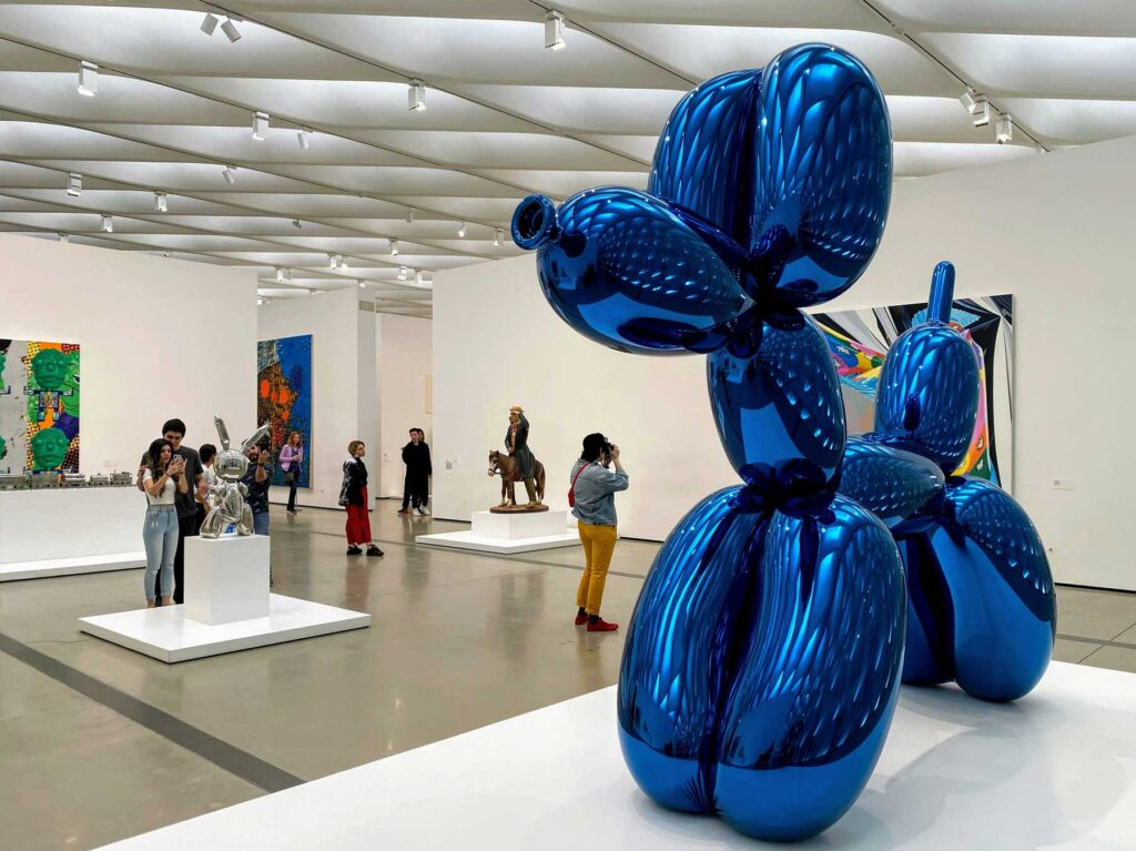 Visitors circulating around a large reflective blue sculpture in a contemporary museum